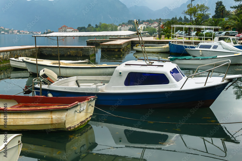 Mooring boats and boats against a background of mountains and houses with red roofs. Sea water with seaweed and raindrops. Beautiful reflection in the water. Mooring boats and boats against a background of mountains and houses with red roofs. Sea water with seaweed and raindrops. Beautiful reflection in the water.
