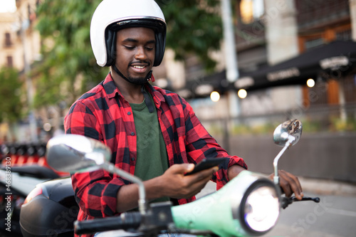 Handsome African man with scooter in the city. Young man using the phone..