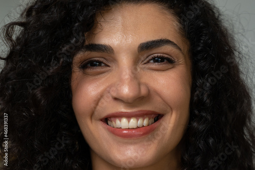 Close-up of the face of a cheerful young mixed-race woman with curly hair in a white shirt, posing and looking at the camera