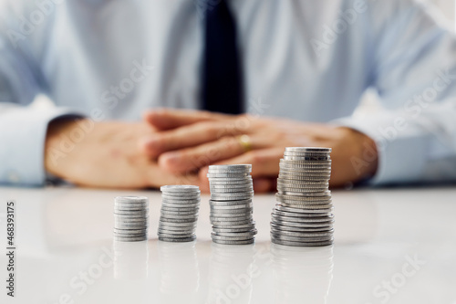 Columns with coins and a man sitting in the background, financial investment concept.