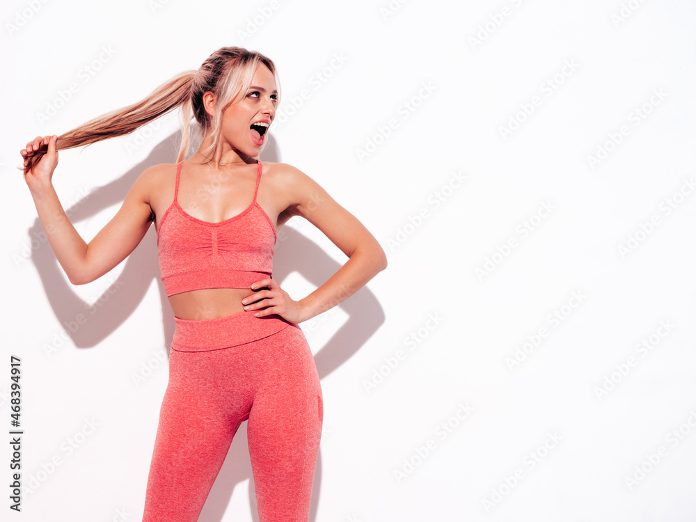 Fitness smiling woman in pink sports clothing. Young beautiful model with perfect body.Female posing near white wall in studio.Cheerful and happy. Stretching out before training.Screaming and shouting Fitness smiling woman in pink sports clothing. Young beautiful model with perfect body.Female posing near white wall in studio.Cheerful and happy. Stretching out before training.Screaming and shouting