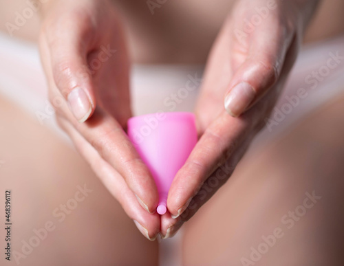 The girl holds in her hands a pink menstrual cup against the background of underwear. Modern silicone medical bowl for collecting discharge during menstruation, close-up