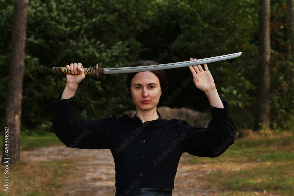 Woman in black classic clothes with katana sword in the forest
