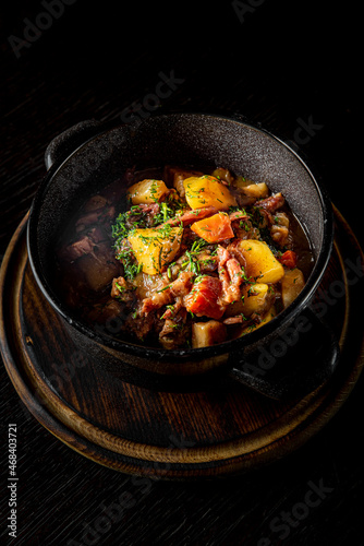 Goulash. Vegetable rague with meat, eggplant, pepper, potato and carrot in black bowl on dark wooden background