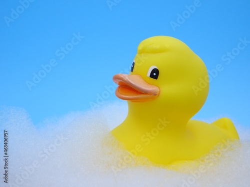 Yellow rubber duck in bath with lots of foam on a blue background.