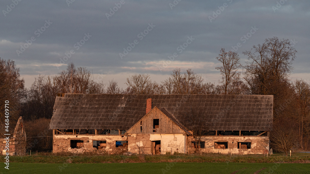 An abandoned old farm house or a big barn with old slate roofing. This very old run down building complex is surrounded by grassland and trees. empty windows and doorway An abandoned old farm house or a big barn with old slate roofing. This very old run down building complex is surrounded by grassland and trees. empty windows and doorway