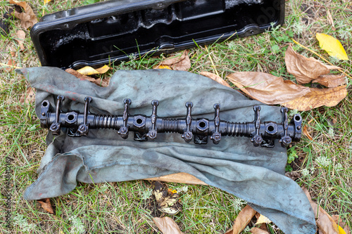Engine part rocker shaft with rocker arms for valves lies on dirty rag on grass. DIY repair on street. breakdown on the way