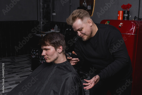 Barber European looking man hairdresser cuts the client with dark hair. Hairdressing