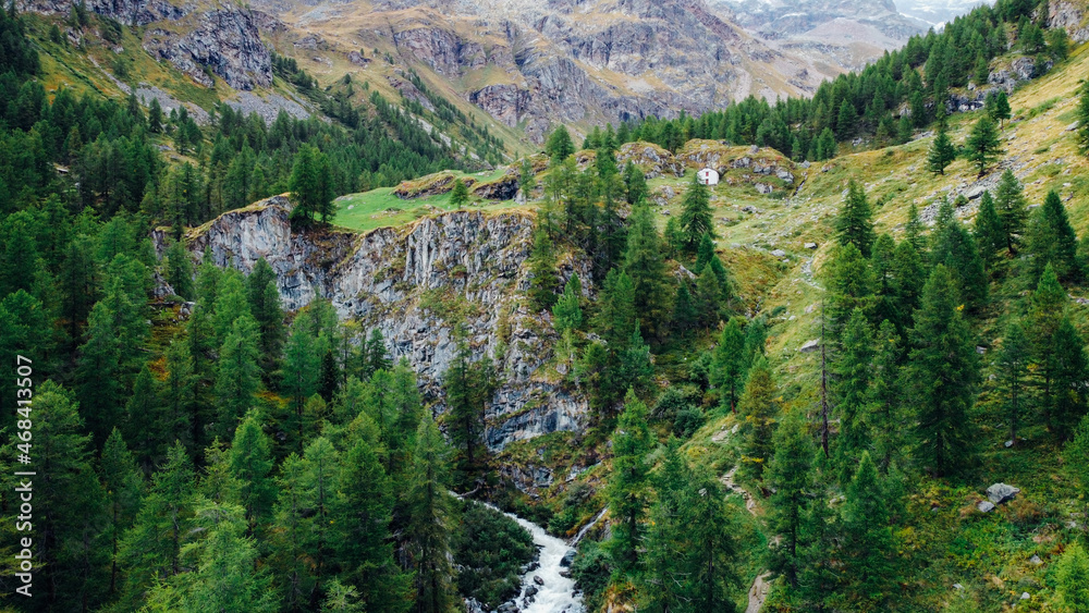 Mountain landscape in Gressoney-Saint-Jean, Aosta Valley region of north-western Italy. Aerial view of green coniferous forest, mountain peaks, river and grasslands in the Italian Alps.