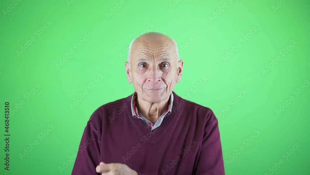 Old gray haired bald man take off dust from sweater and smiling looking to camera standing in studio with green screen Old gray haired bald man take off dust from sweater and smiling looking to camera standing in studio with green screen