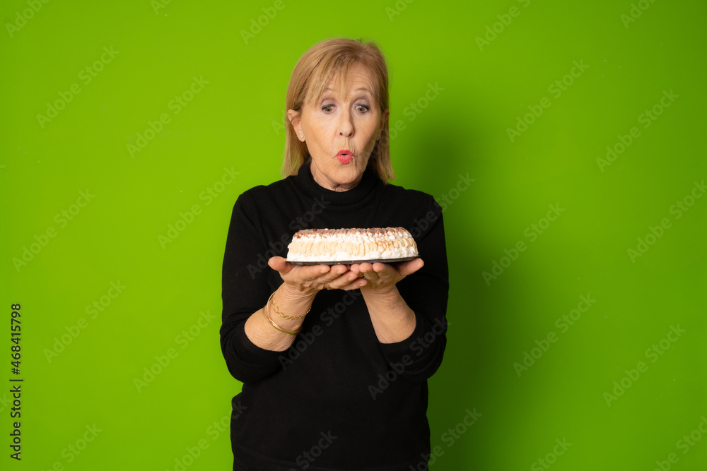Studio shot of a mature amazed lady holding a cake and looking at camera isolated on green background Studio shot of a mature amazed lady holding a cake and looking at camera isolated on green background
