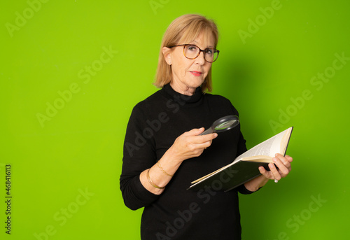 Image of aged woman with an open book isolated over green background.