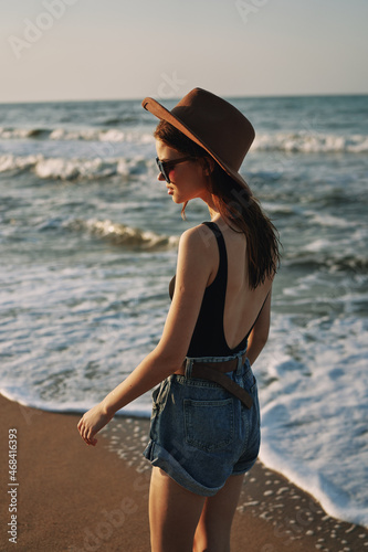 cheerful woman in sunglasses and a hat walks along the ocean