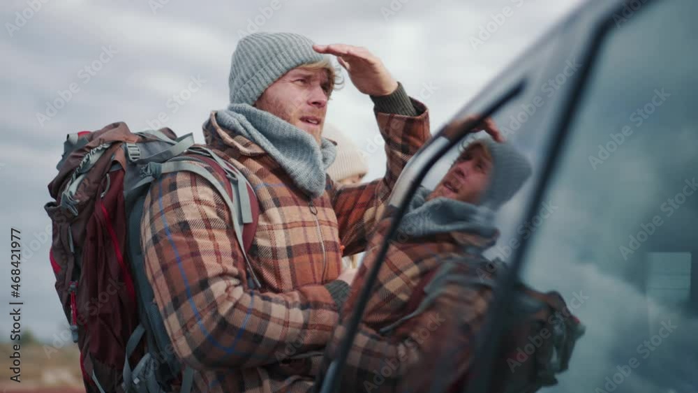 Handsome blond man tourist in hat rubbing hands and looking into the distance near car Handsome blond man tourist in hat rubbing hands and looking into the distance near car