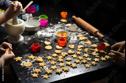 Children prepare star-shaped birthday cookies on a dark kitchen table. Family joint activity in the kitchen at home. View from above.