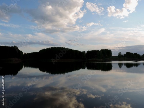 View of the mirror surface of the lake  the opposite shore and the blue sky with clouds at sunset.