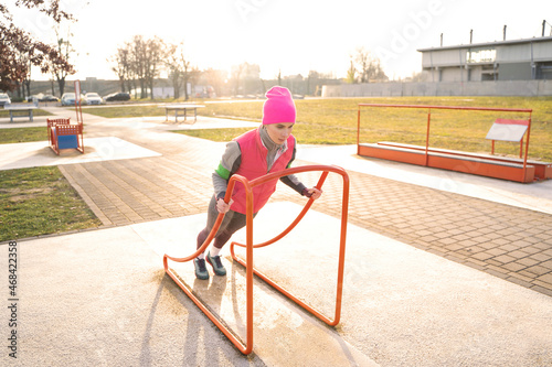 Fototapeta Naklejka Na Ścianę i Meble -  Young caucasian athletic fit woman in warm colorful fitness clothes doing push-ups on gym workout machine outdoors on sports ground on autumn, winter or spring early morning sunrise in Dresden