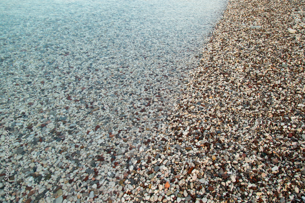 The beach is made of pebbles, the seashore, small colored pebbles in the water. Background, copy space.
