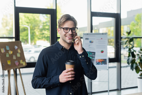 Smiling programmer with coffee talking on smartphone in office