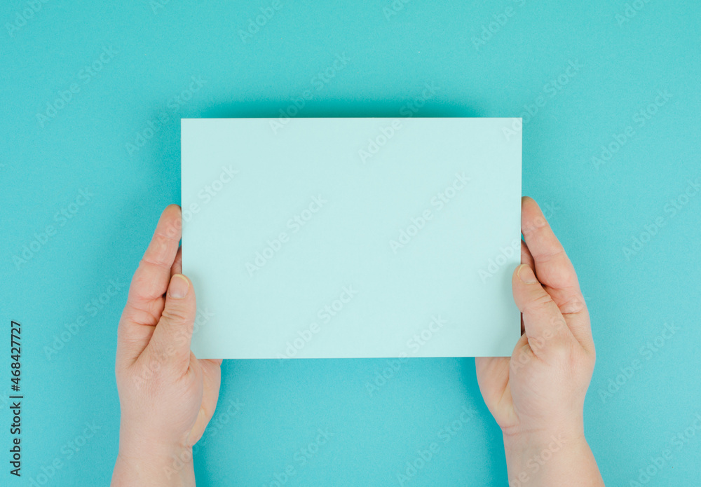 Woman holds a blank sheet of paper, blue colored background, empty copy space for text, minimalism Woman holds a blank sheet of paper, blue colored background, empty copy space for text, minimalism