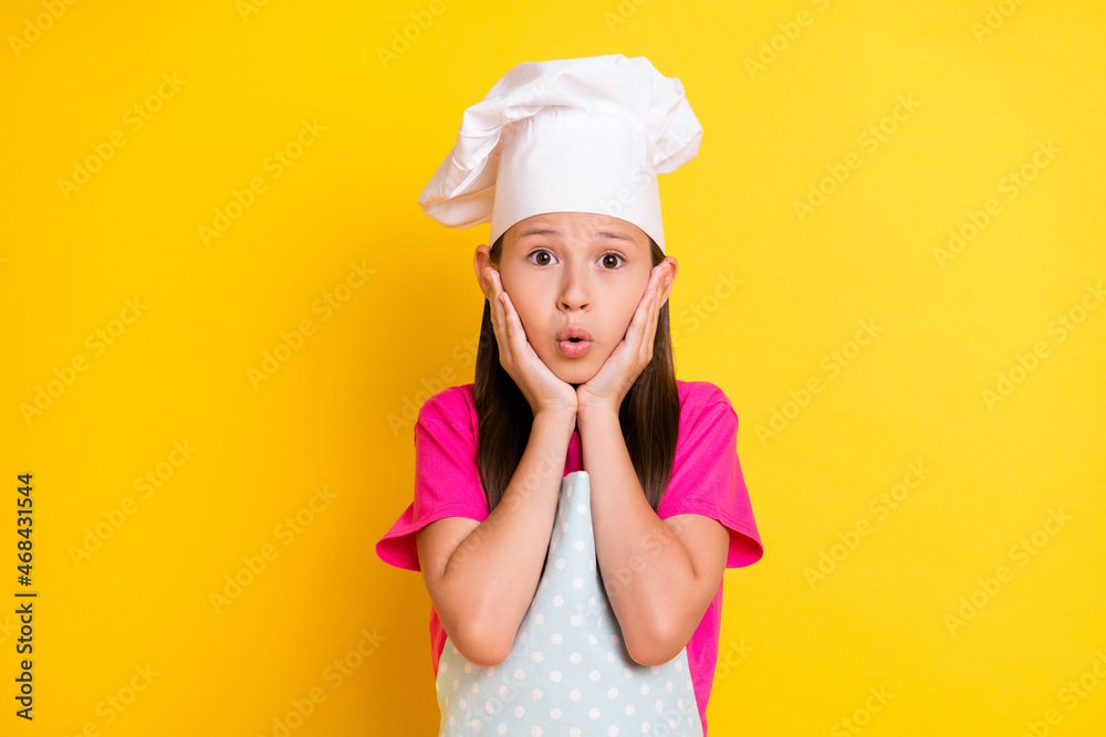 Photo of crazy speechless stunned girl hands cheeks open mouth wear white apron hat isolated yellow color background Photo of crazy speechless stunned girl hands cheeks open mouth wear white apron hat isolated yellow color background