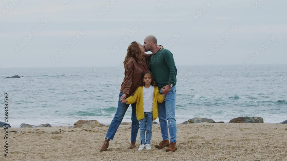 Young happy family is spending time on ocean beach, parents are kissing each other, holding their daughter’s arms, looking at camera, live in harmony and love, Slow motion. Young happy family is spending time on ocean beach, parents are kissing each other, holding their daughter’s arms, looking at camera, live in harmony and love, Slow motion.