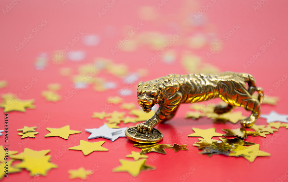 A bronze figure of a tiger with coin - symbol of the Chinese new year 2022 on a red background, gold and silver stars copy space. Wishes of good luck, financial well-being and wealth
