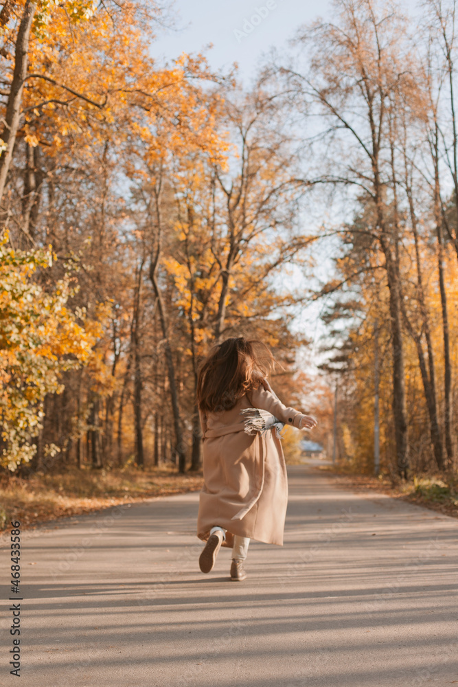 Young beautiful woman in beige coat happily running on the road in autumn park Young beautiful woman in beige coat happily running on the road in autumn park
