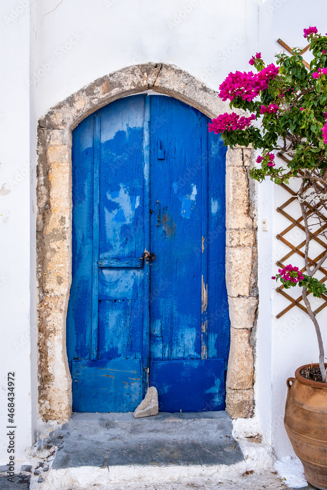 Fototapeta premium Greek island Kythira Chora, Greece. Blue wooden door and red bougainvillea on whitewashed wall.