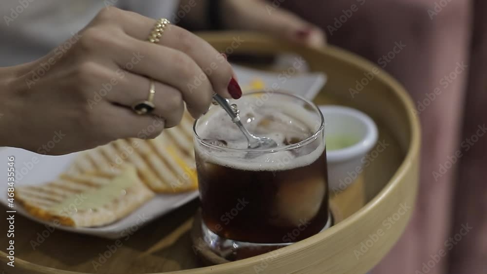 Joven bate lentamente con cuchara de metal a un te helado en vaso de cristal