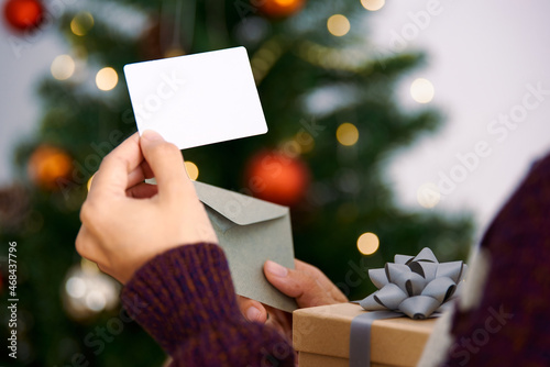 Hand holding mockup christmas greeting card and gift box for invitation design on christmas tree background.