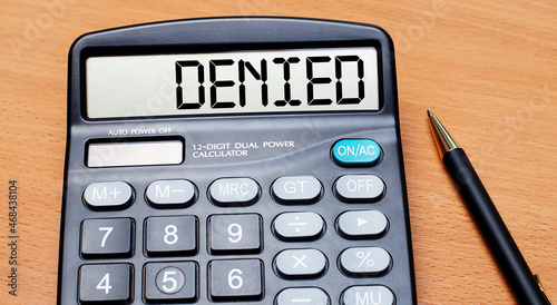 On a wooden table there is a black pen and a calculator with the text DENIED. Business concept