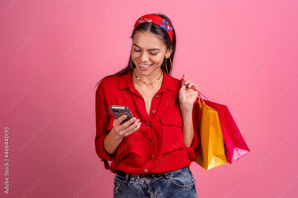 hispanic beautiful woman in red shirt smiling holding holding shopping bags and smartphone