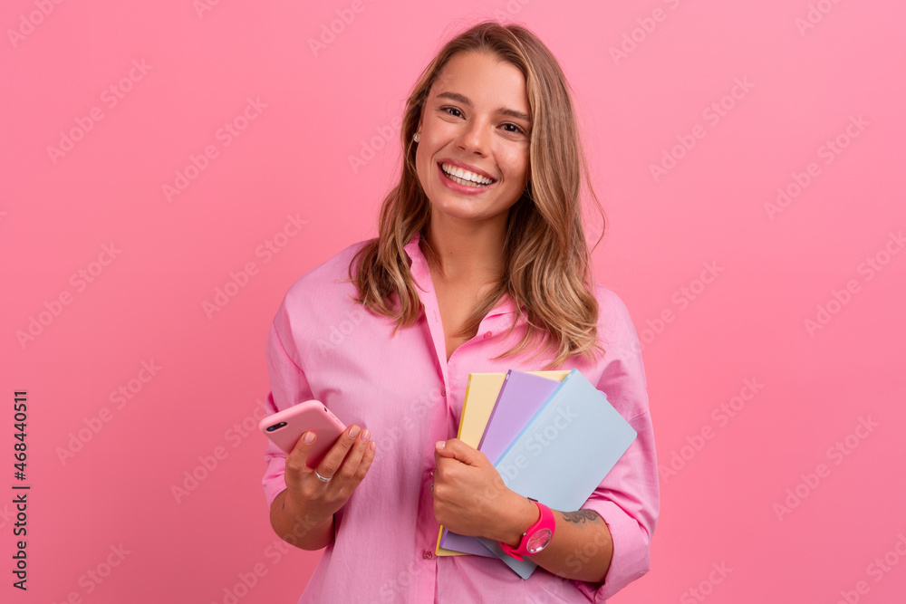 blond pretty woman in pink shirt smiling holding holding notebooks and using smartphone blond pretty woman in pink shirt smiling holding holding notebooks and using smartphone