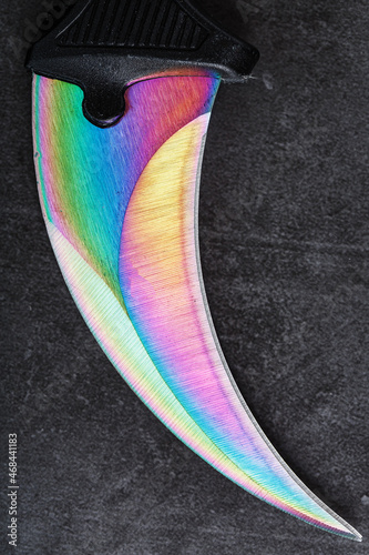 The sharp blade of the Kerambit knife made of steel is multicolored in close-up on a dark background. photo