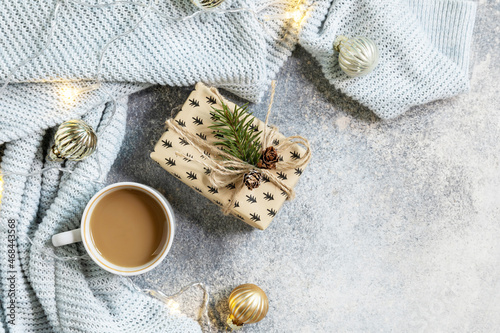 Christmas composition with cup of coffee, knitted blanket, garland and gift on a gray background. Winter, Christmas concept. Flat lay, top view, copy space.