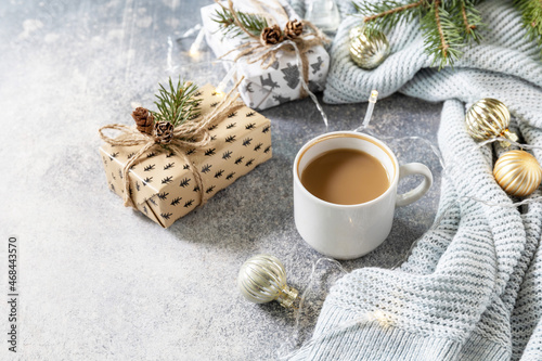 Christmas composition with cup of coffee, knitted blanket, garland and gift on a gray background. Winter, Christmas concept. Copy space.