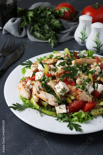 Salad with bulgur, baked chicken, bell pepper, basil and feta on white plate on dark background