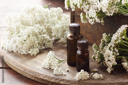 Yarrow herb essential oil or extract in amber bottles with milfoil blossoms on wooden rustic background, closeup, natural cosmetics and naturopathy concept photo