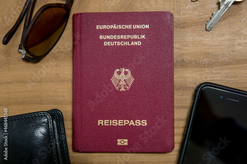 german passport on a wooden table surrounded by sunglasses, a mobile phone, keys and a wallet