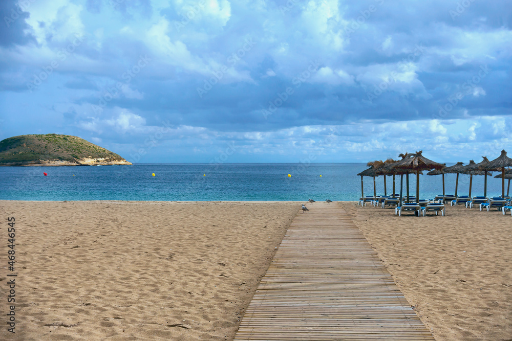 wooden walkway on a sandy beach against the backdrop of the sea, straw umbrellas and plastic sunbeds