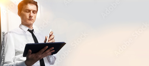 Banner is a businessman working on his digital tablet. A serious man looks at the tablet from the window sunlight. The concept of a work routine. High quality photo