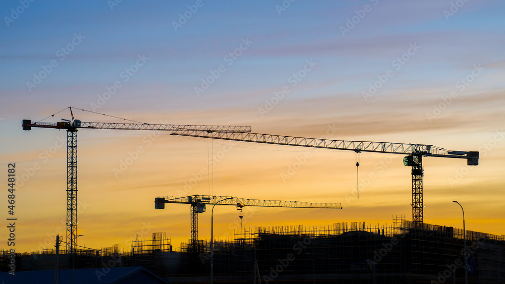 Silhouettes of construction cranes, orange sunset on the background