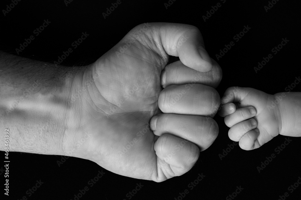 Newborn's fist in front of dad's fist on black background Newborn's fist in front of dad's fist on black background