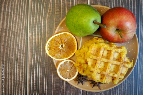 pumpkin Belgian gluten-free waffles lie on a brown plate with a dry slice of lemon, pumpkin on a background of yellow maple leaves on a wooden table with a pear and an apple. top view. gluten-free