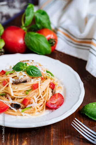 Fresh pasta with spaghetti, tomato, mushrooms, basil and parmesan cheese in white plate on a wooden background with ingredients in background