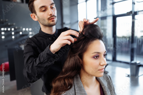 The master does hair styling in a beauty salon. Young woman preparing for a date.