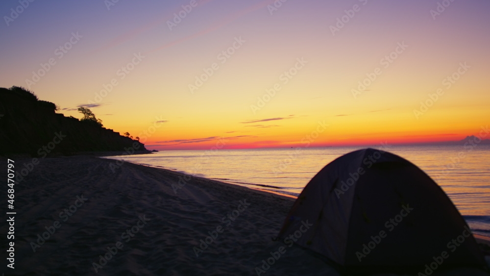 Camp tent at dark sand beach at golden sunrise morning. Campsite ocean seashore