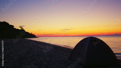 Camp tent at dark sand beach at golden sunrise morning. Campsite ocean seashore