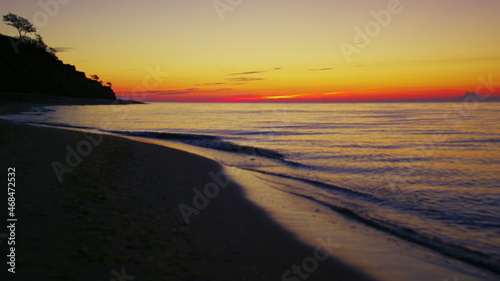 Lake coastline at orange sunset dawn. Dark sea beach with mountain silhouette
